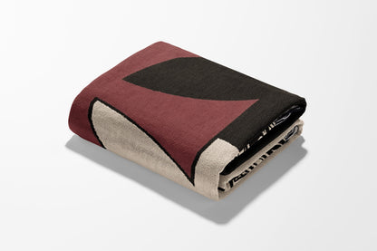 Folded blanket with geometric pattern in maroon, black, and cream.