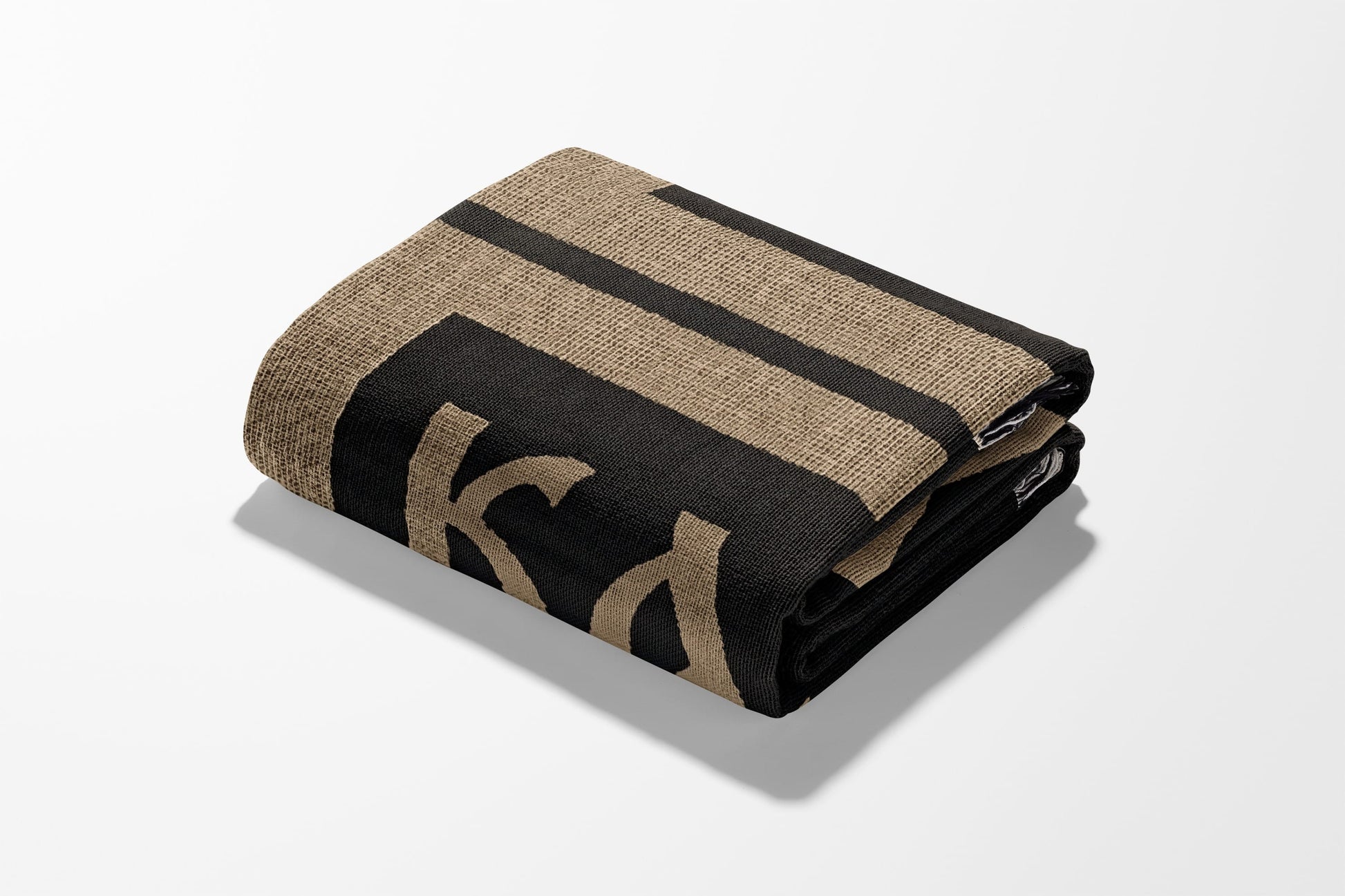 Folded blanket with black and tan stripes and a large black "K" graphic.