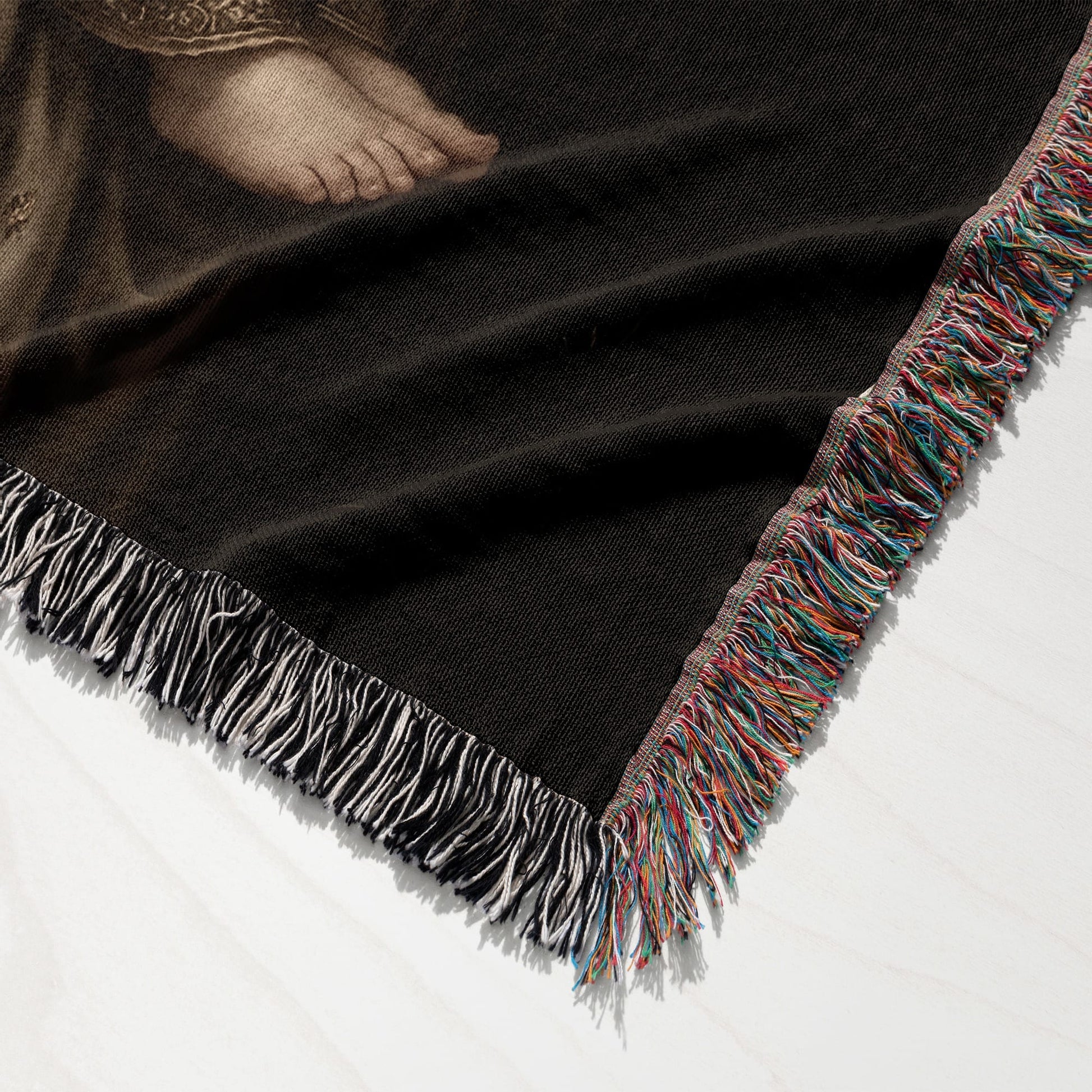 Woven blanket with a detailed fringe and a section of a painting showing a human foot.