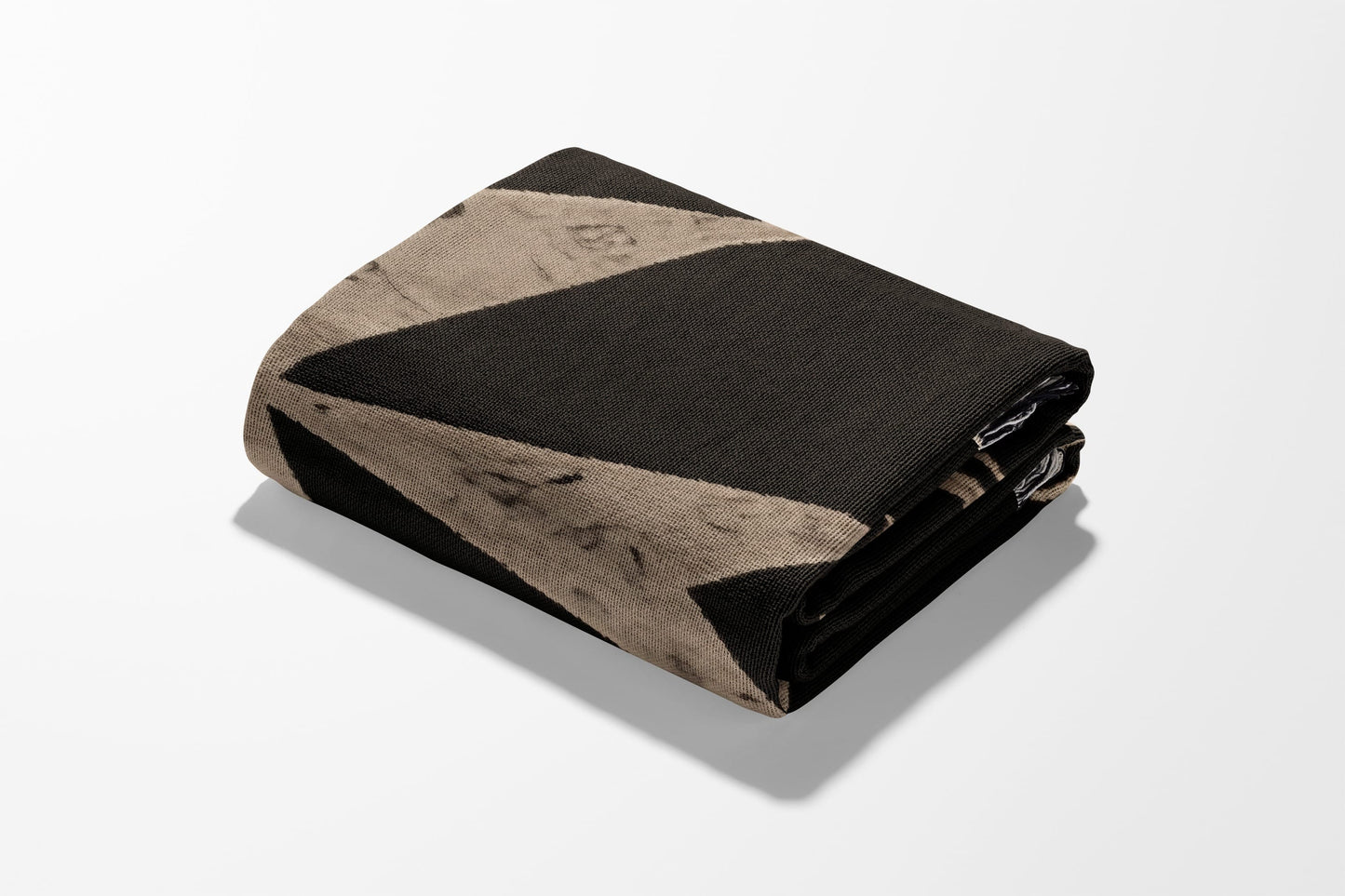 Folded blanket with a black and tan geometric pattern against a white background.