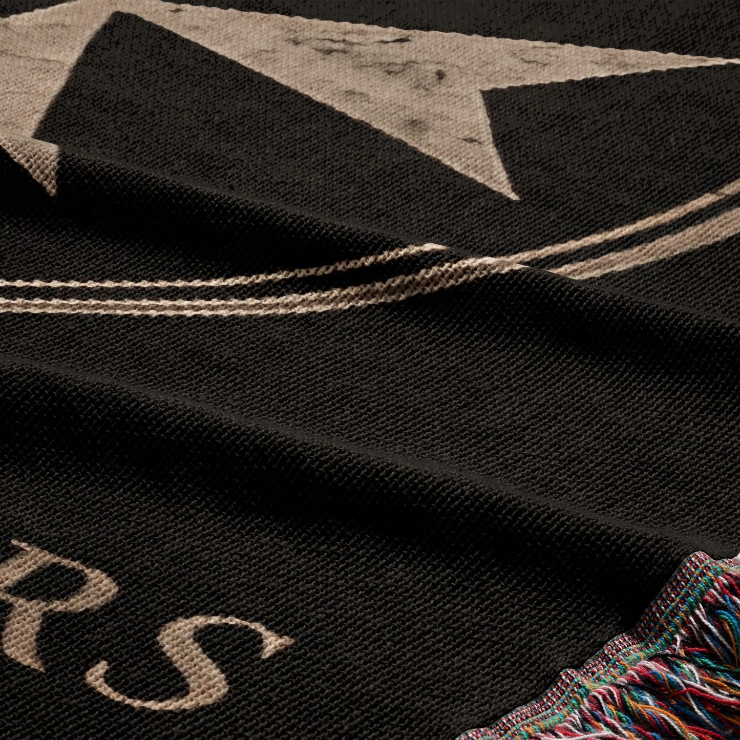 Black textile with a large faded white graphic and fringe trim.