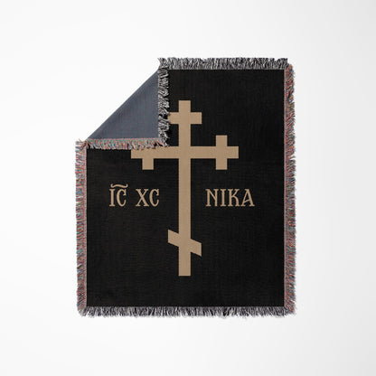 Black throw blanket with tan IC XC NIKA cross design and fringed edges.