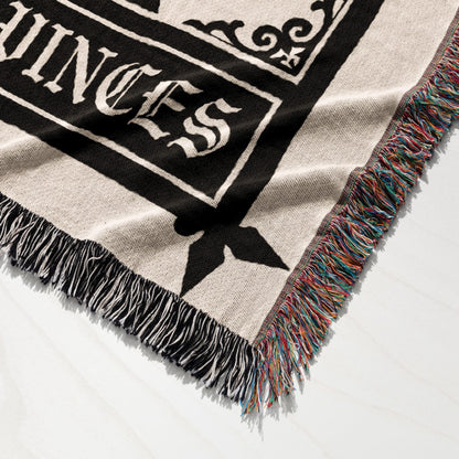 Close-up of a woven blanket with intricate black design and colorful fringed edges.