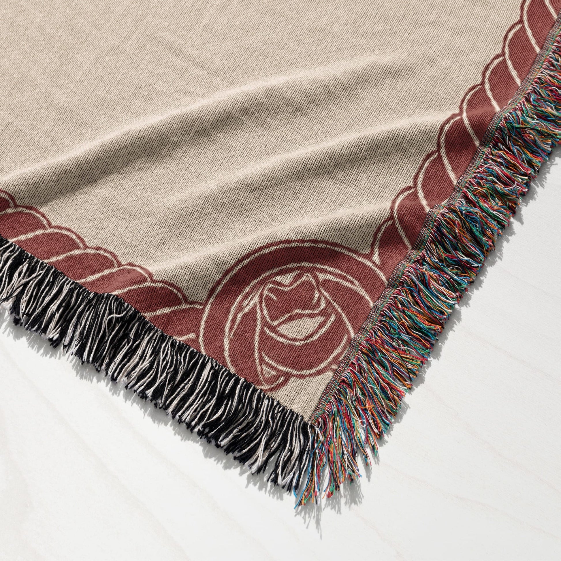 Woven throw blanket with fringed edges and a rose design.
