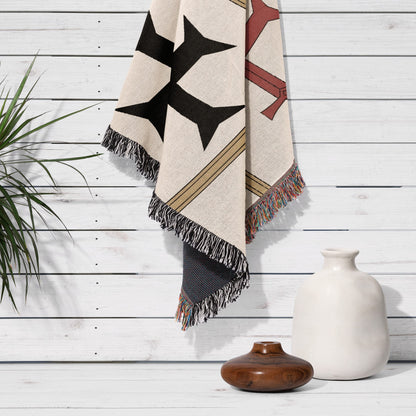 Textile blanket with geometric pattern and fringed edges draped over a white wooden wall.