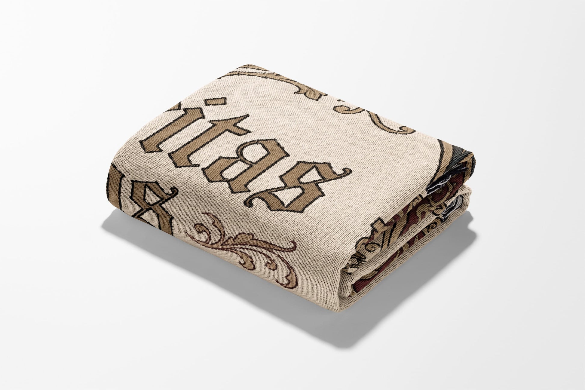 Folded cream blanket with gothic "Kitas" text and scrolling brown vine pattern.