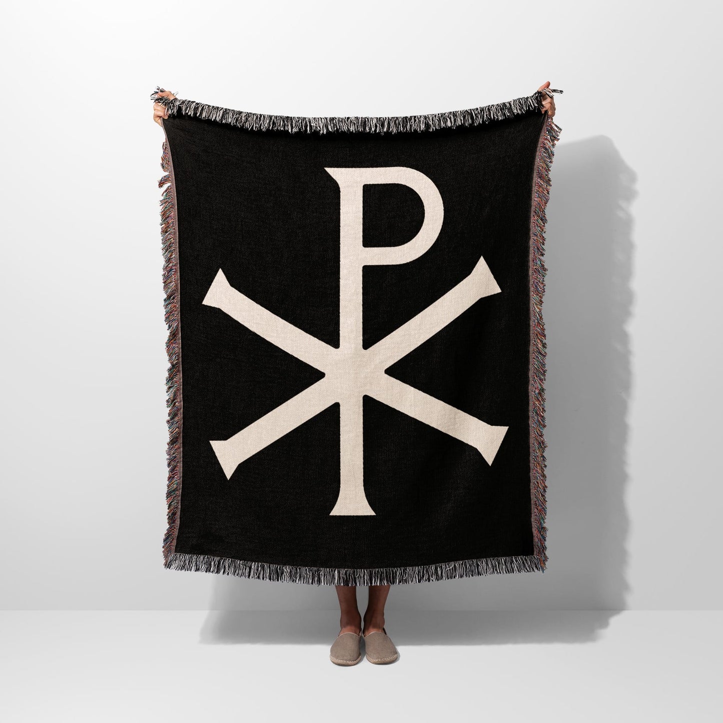 Black throw blanket with beige Chi Rho symbol and fringe.