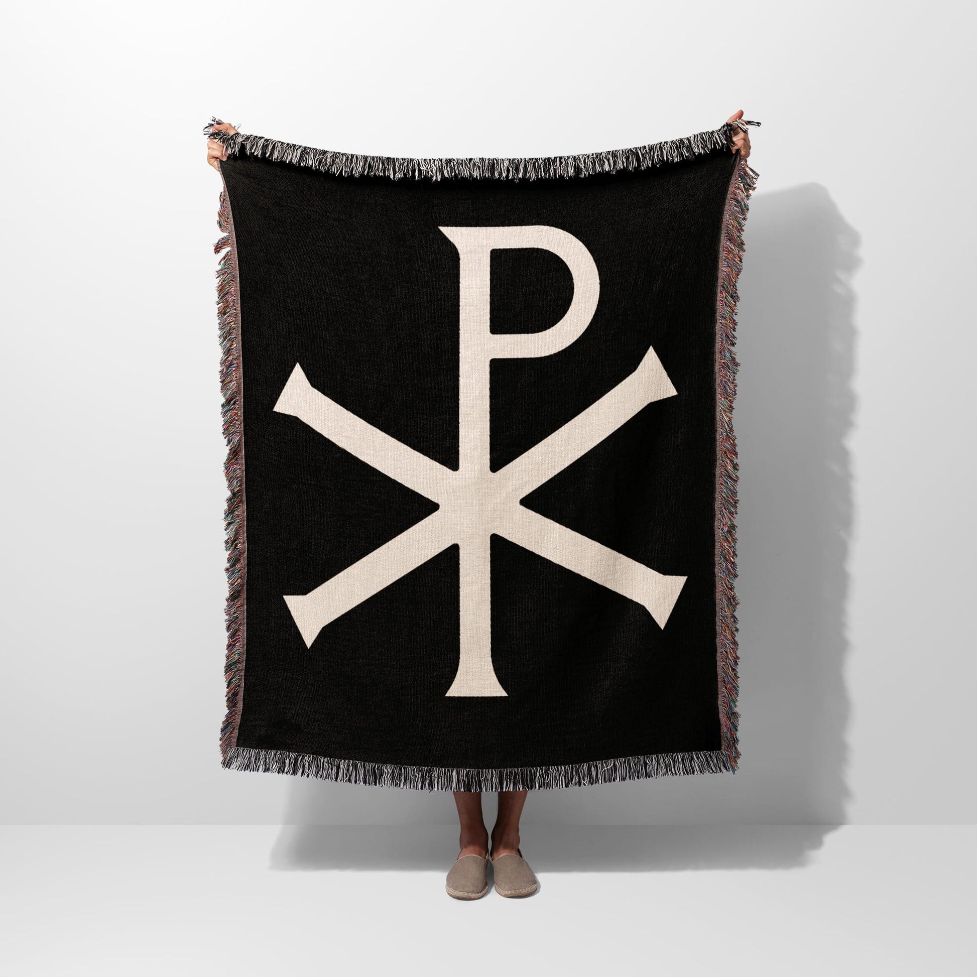 Black throw blanket with beige Chi Rho symbol and fringe.