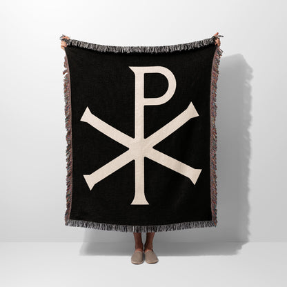 Black throw blanket with beige Chi Rho symbol and fringe.