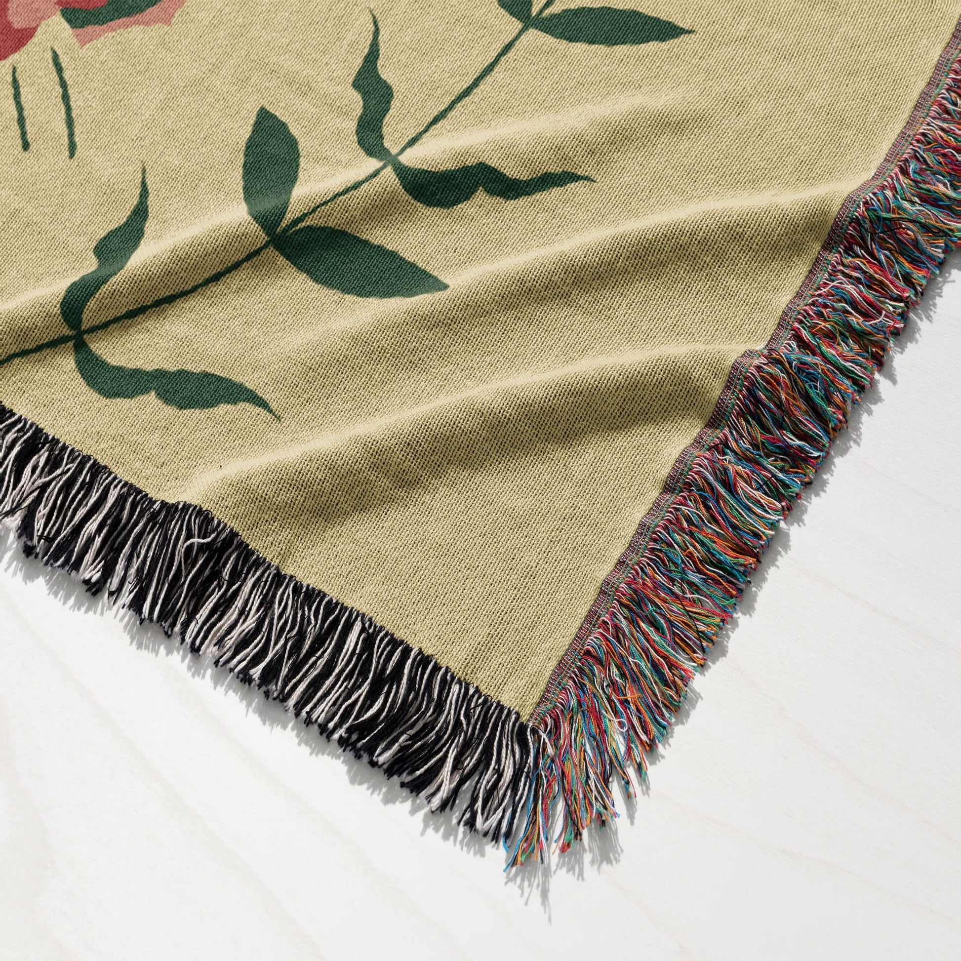 Tan woven throw blanket with a large green floral pattern and fringed edges.