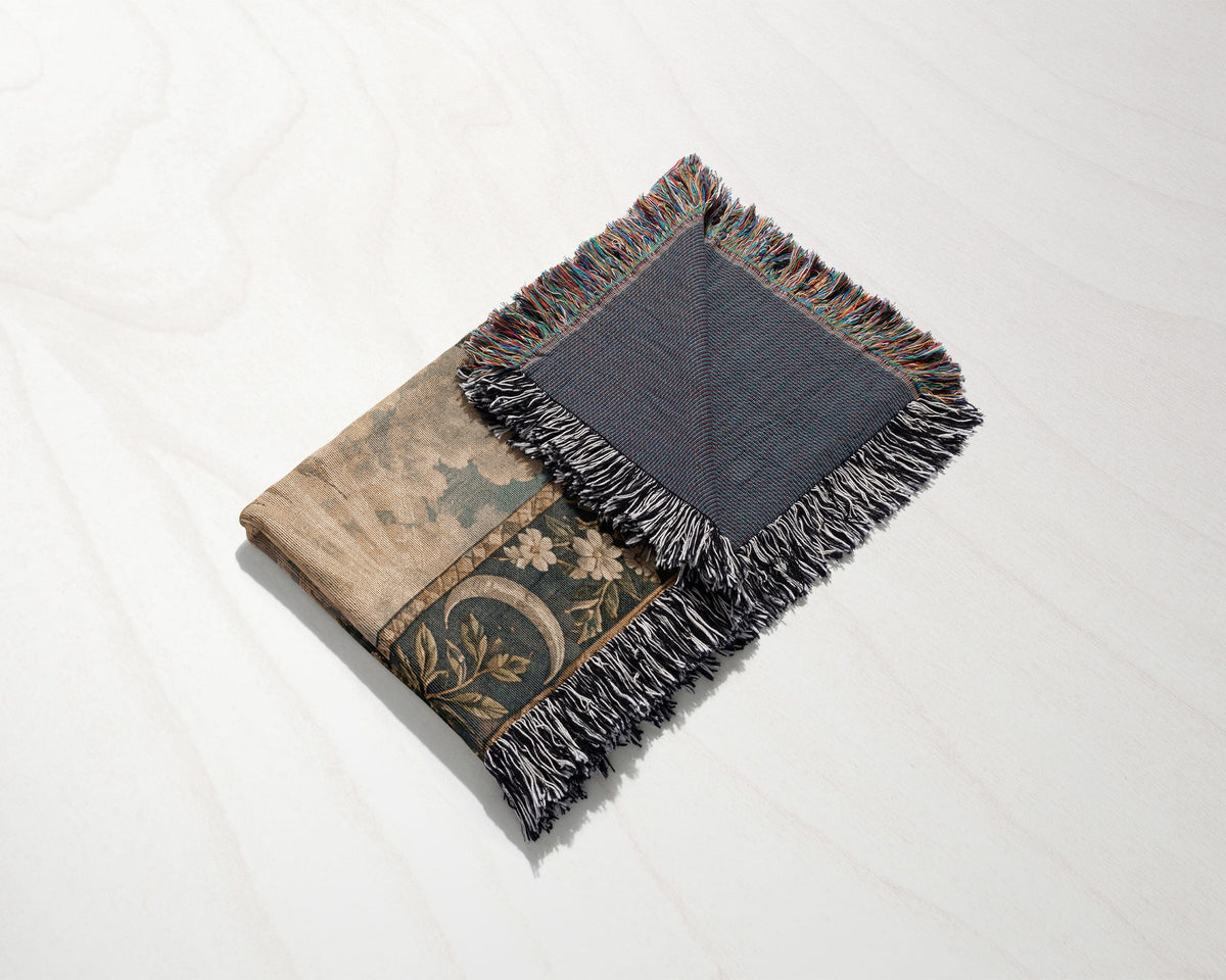 A folded woven blanket with fringed edges, featuring an earthy floral and botanical pattern on a light surface.