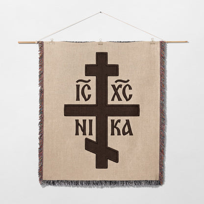 Brown Orthodox cross with Greek lettering on a woven wall hanging.