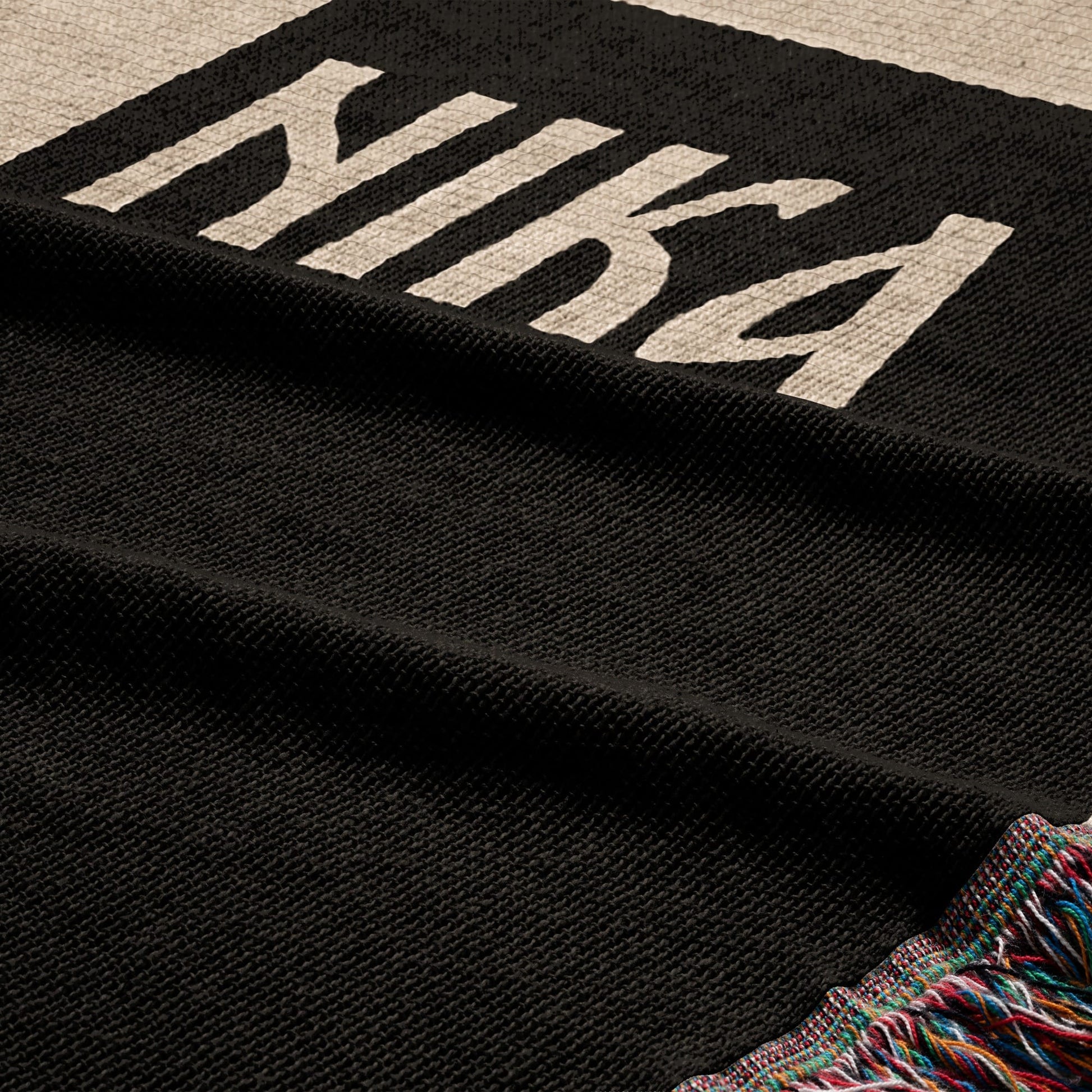 Black woven blanket with white "NIKE" text and a colorful fringed edge.