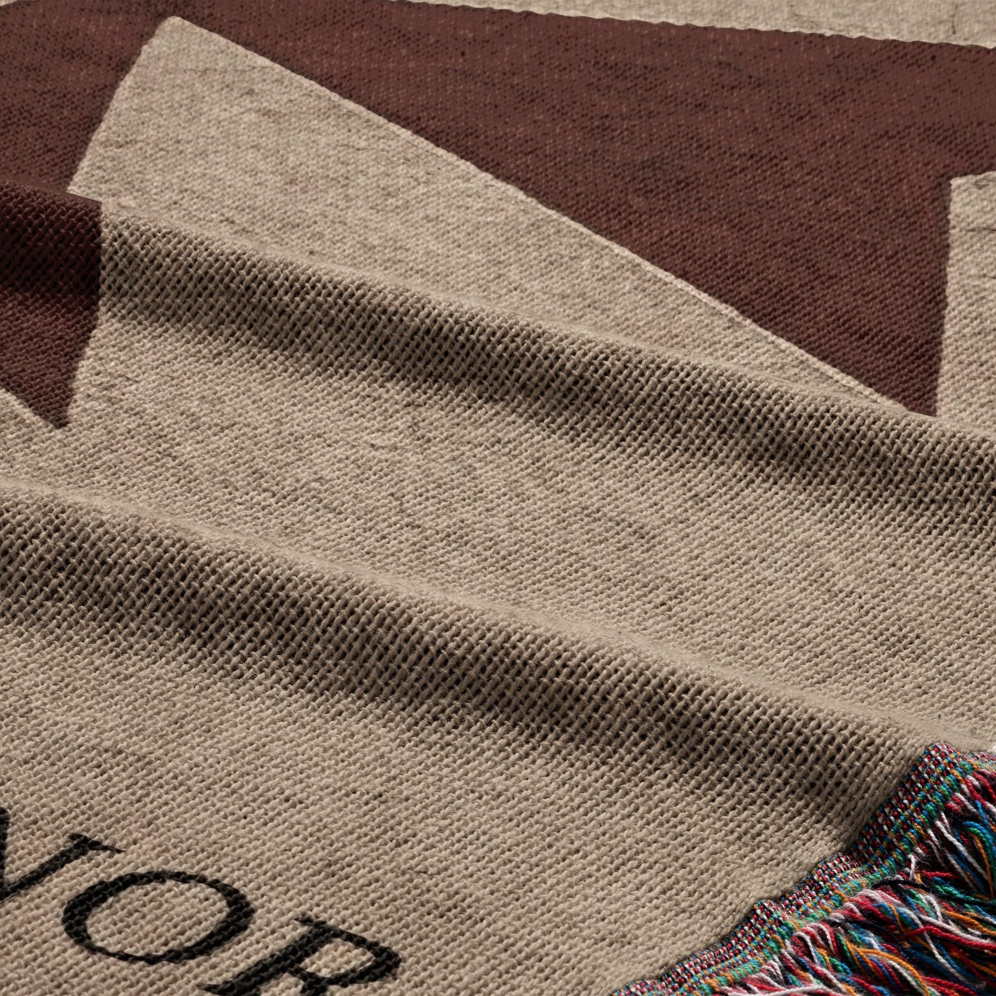 Close-up of tan blanket with brown stripes and colorful fringe, "VOR" text visible.