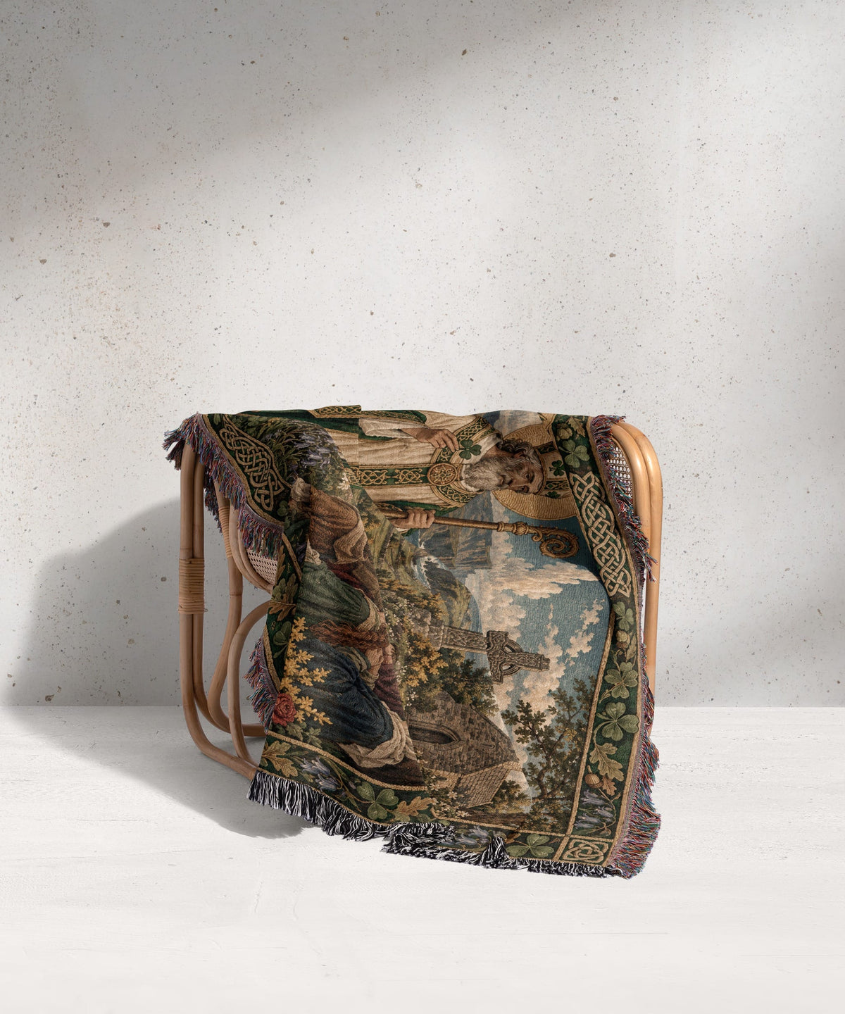 A woven tapestry blanket featuring an Irish landscape scene draped over a rattan chair.