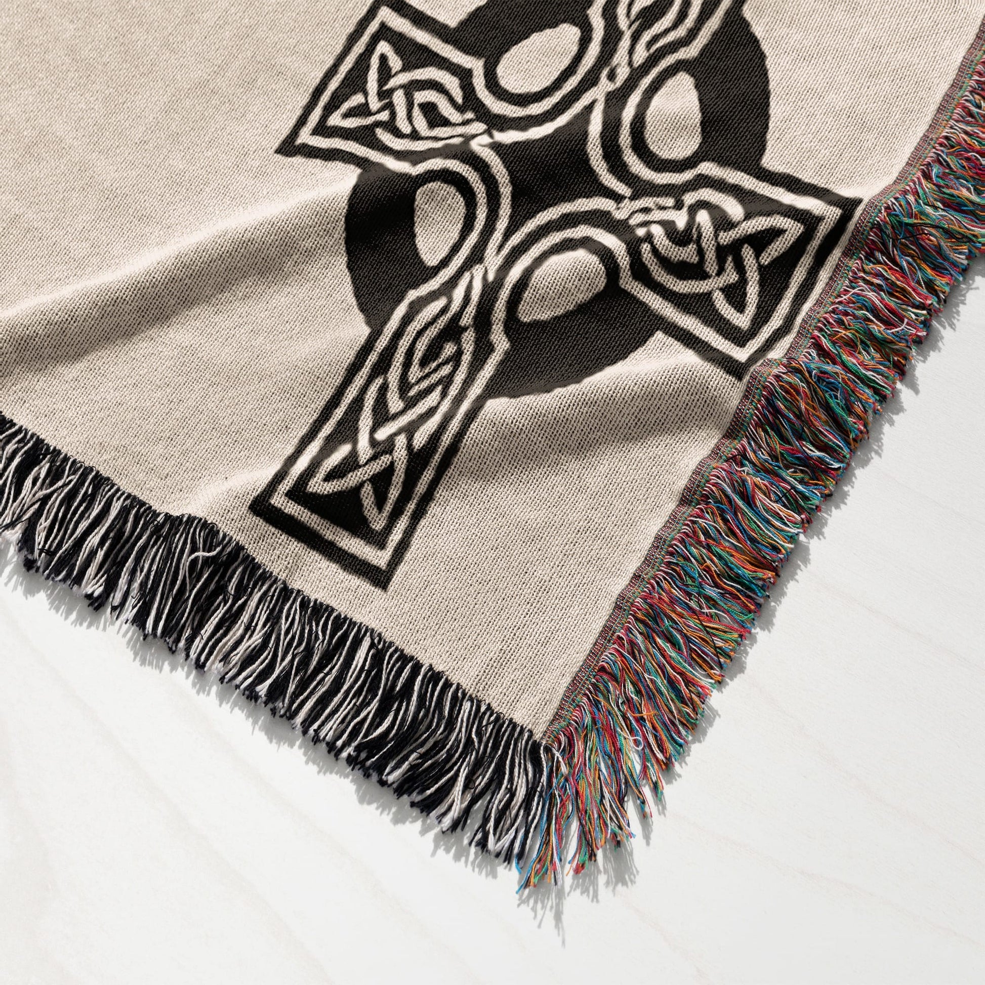 Beige throw blanket with black Celtic knot design and fringed edges.