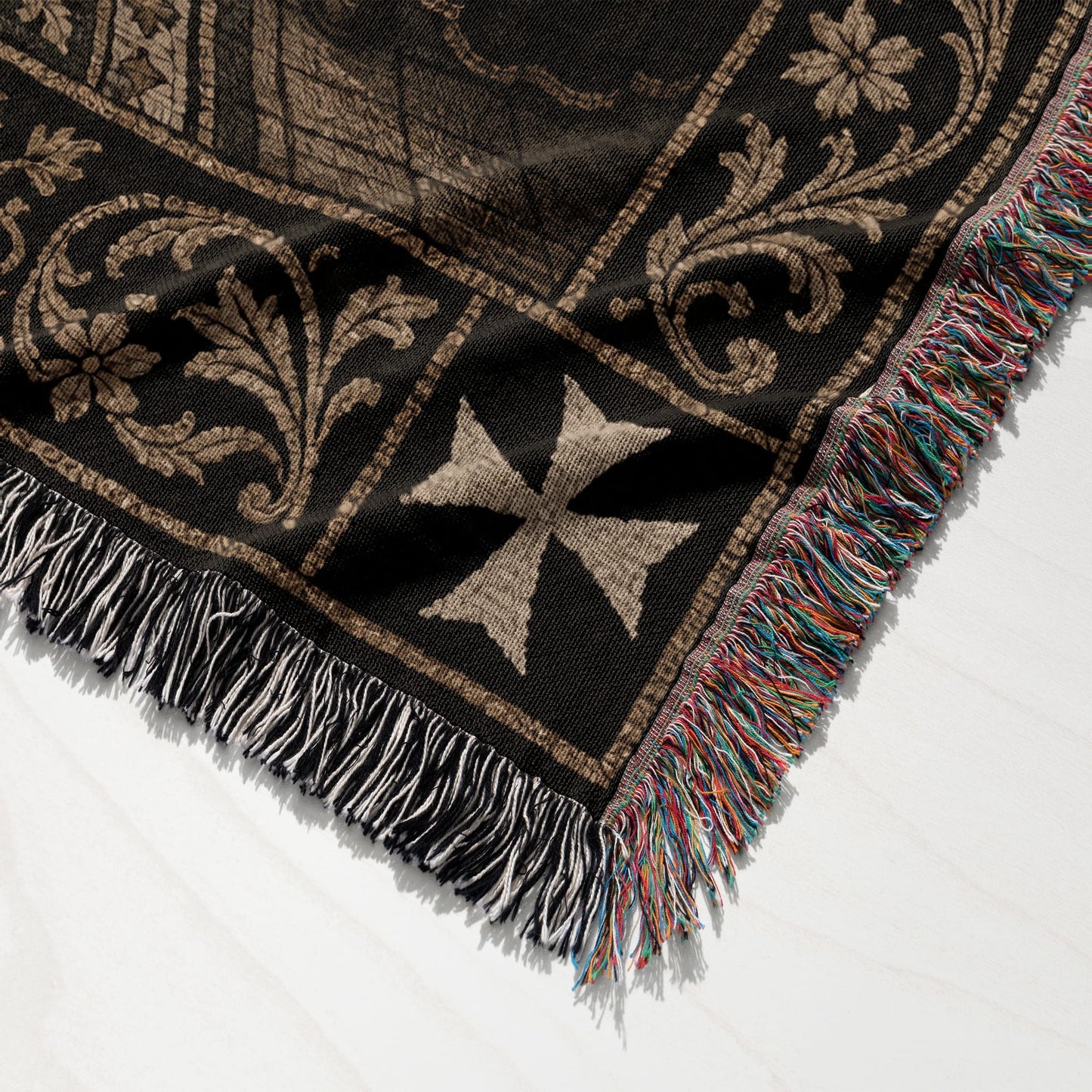 Black woven throw blanket with Maltese cross pattern and colorful fringe.