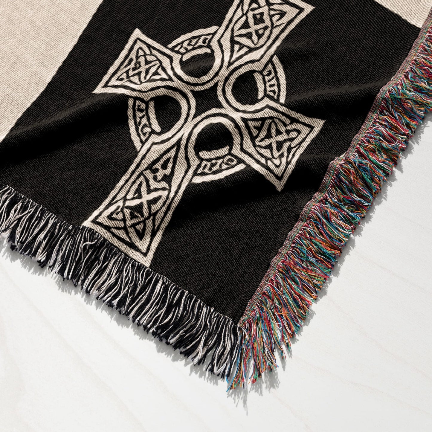 Black woven blanket with white Celtic knot cross and colorful fringed edges.