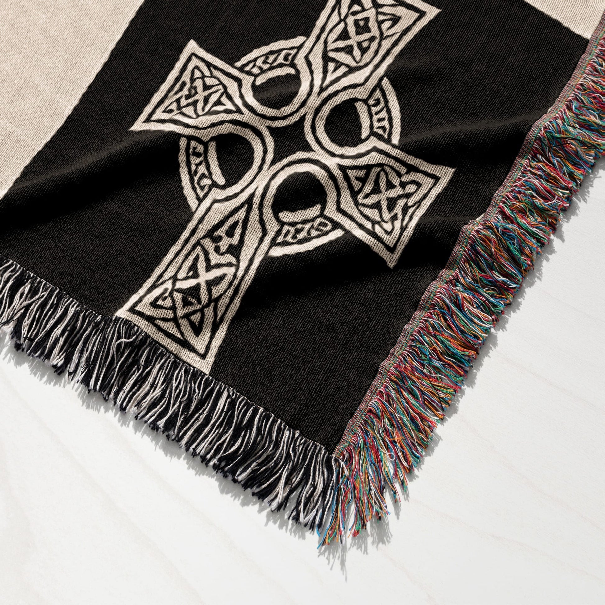 Black woven blanket with white Celtic knot cross and colorful fringed edges.