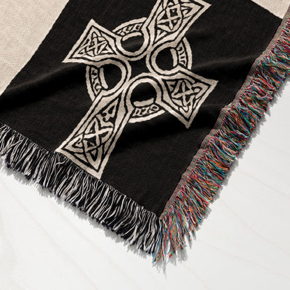 Black woven blanket with white Celtic knot cross and colorful fringed edges.
