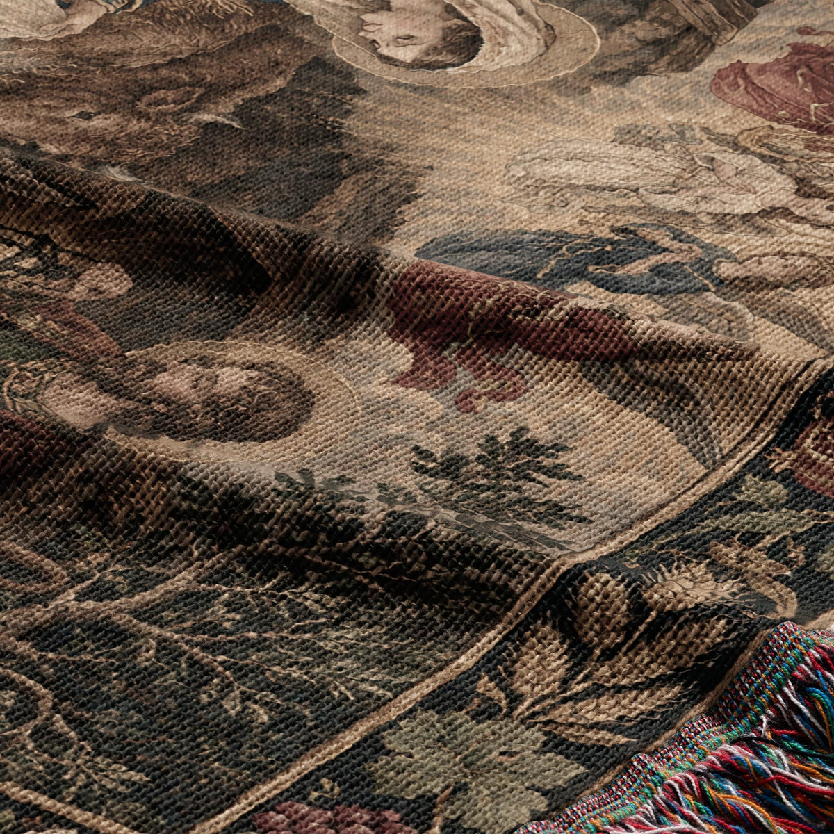 A folded, woven textile featuring a vintage-style historical scene with earthy tones and decorative fringe.
