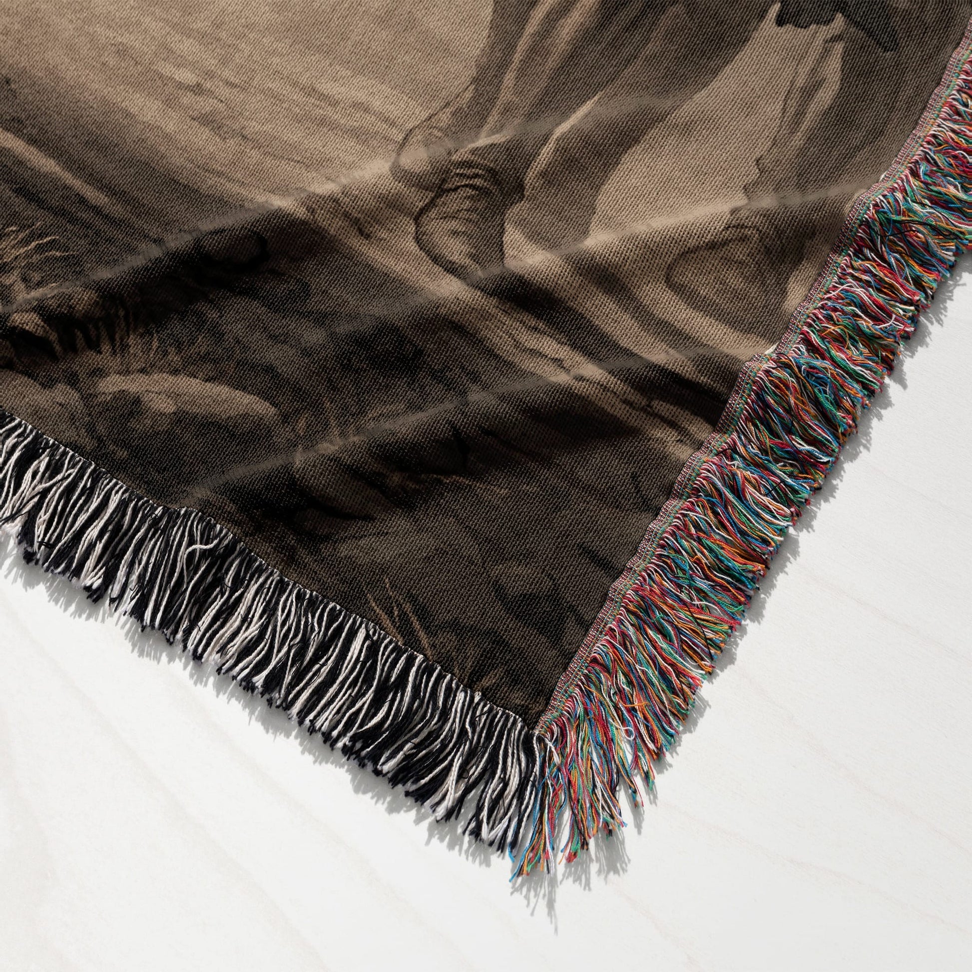 Woven throw blanket with fringed edges, featuring a dark abstract pattern.
