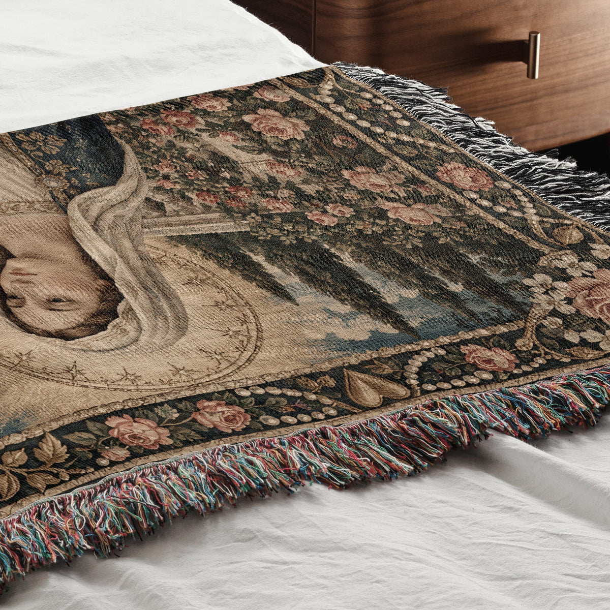 A woven blanket featuring a renaissance art portrait of a woman amidst floral and botanical motifs rests on a white bed.