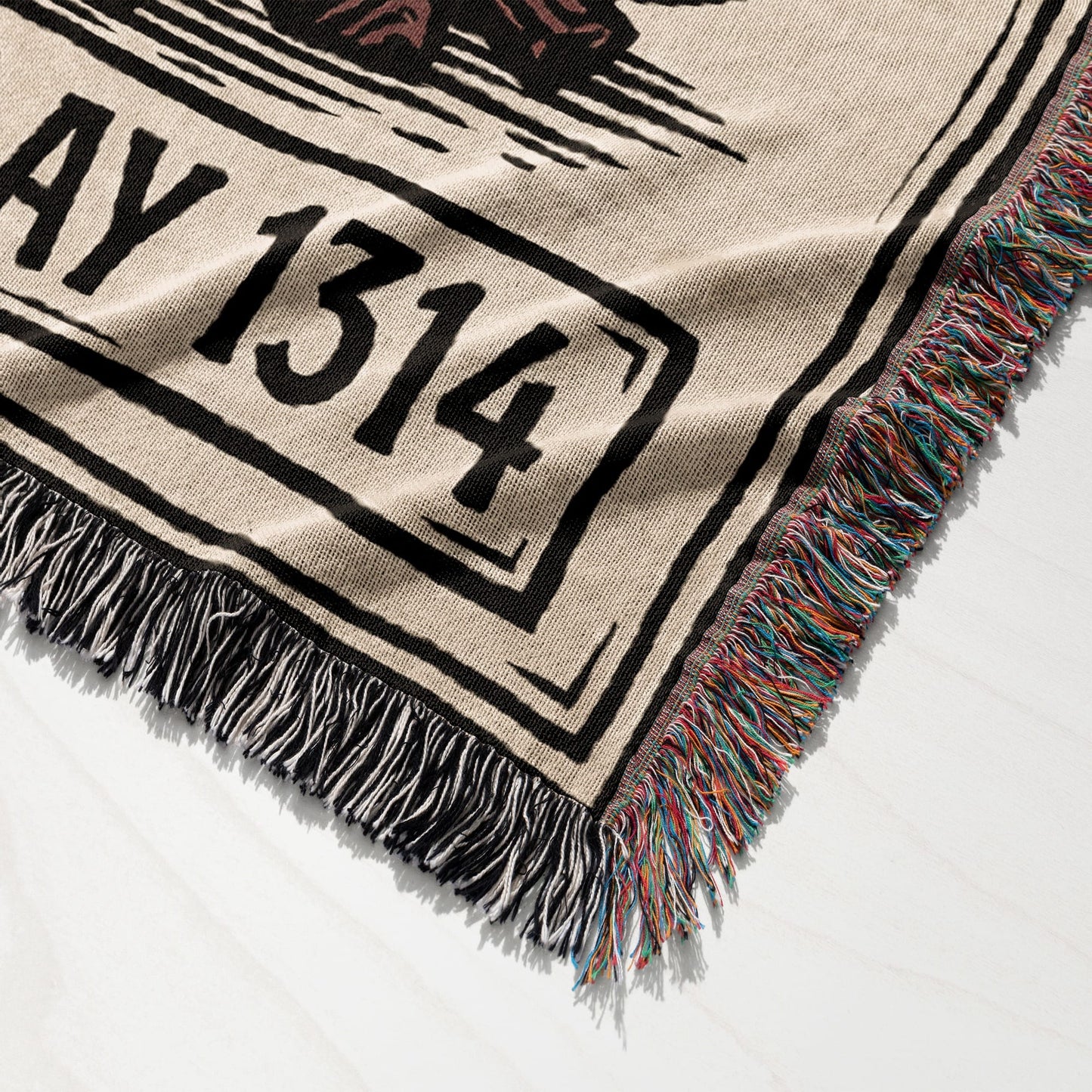 Woven throw blanket with fringe and the text "AY 1314" on a white surface.