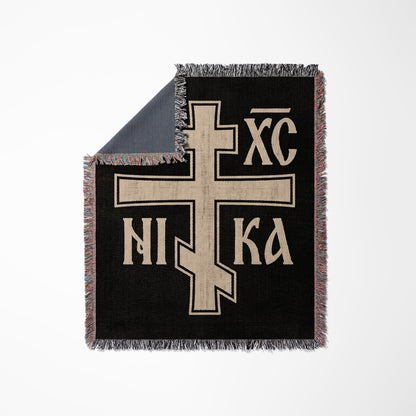 Black throw blanket with a large beige Orthodox Christian cross symbol.