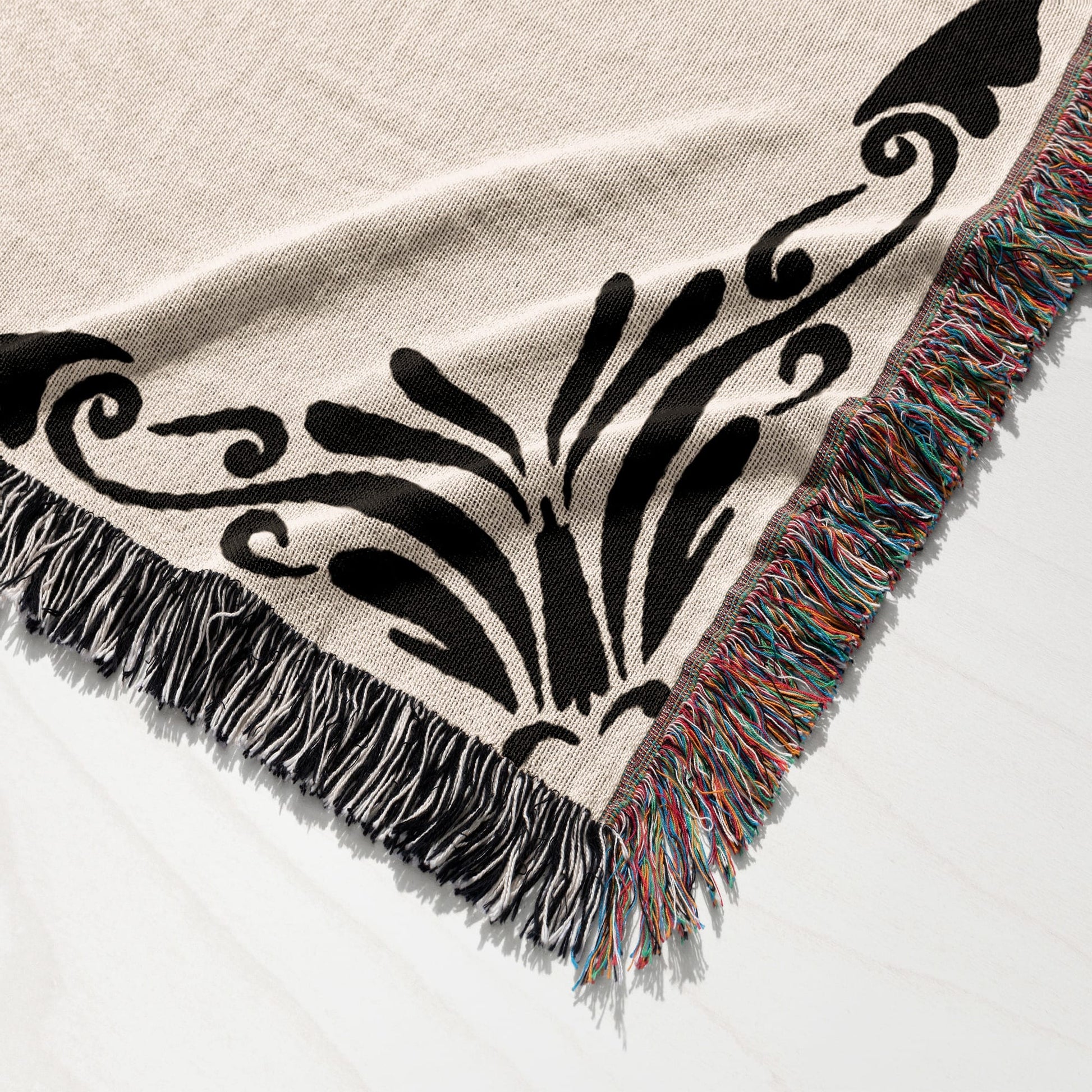 Woven blanket with black floral design and multicolored fringed edges.