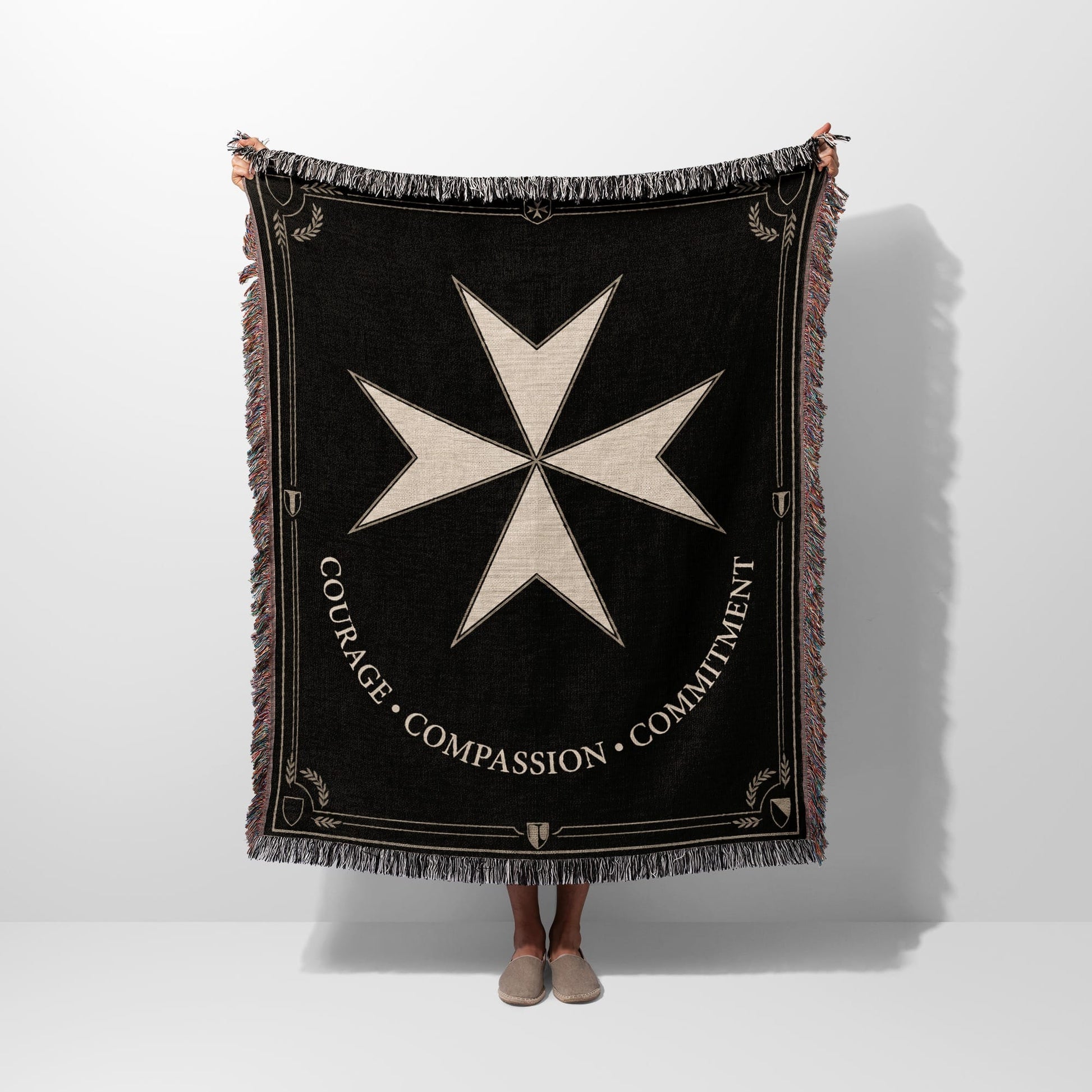 Black blanket with white Maltese cross and "COURAGE COMPASSION COMMITMENT" text.