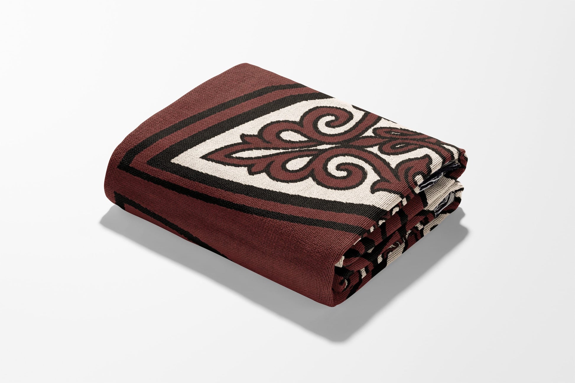 Folded maroon blanket with intricate cream and black swirl pattern.