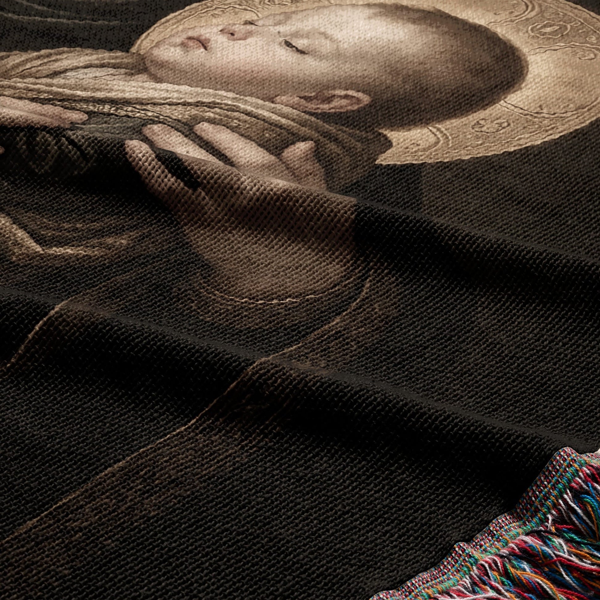 Tapestry detail of a sleeping infant with a halo, dark background, fringed edge.