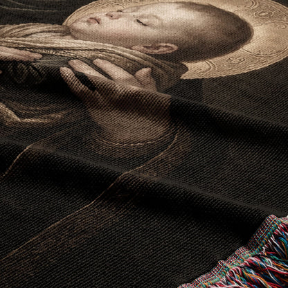 Tapestry detail of a sleeping infant with a halo, dark background, fringed edge.