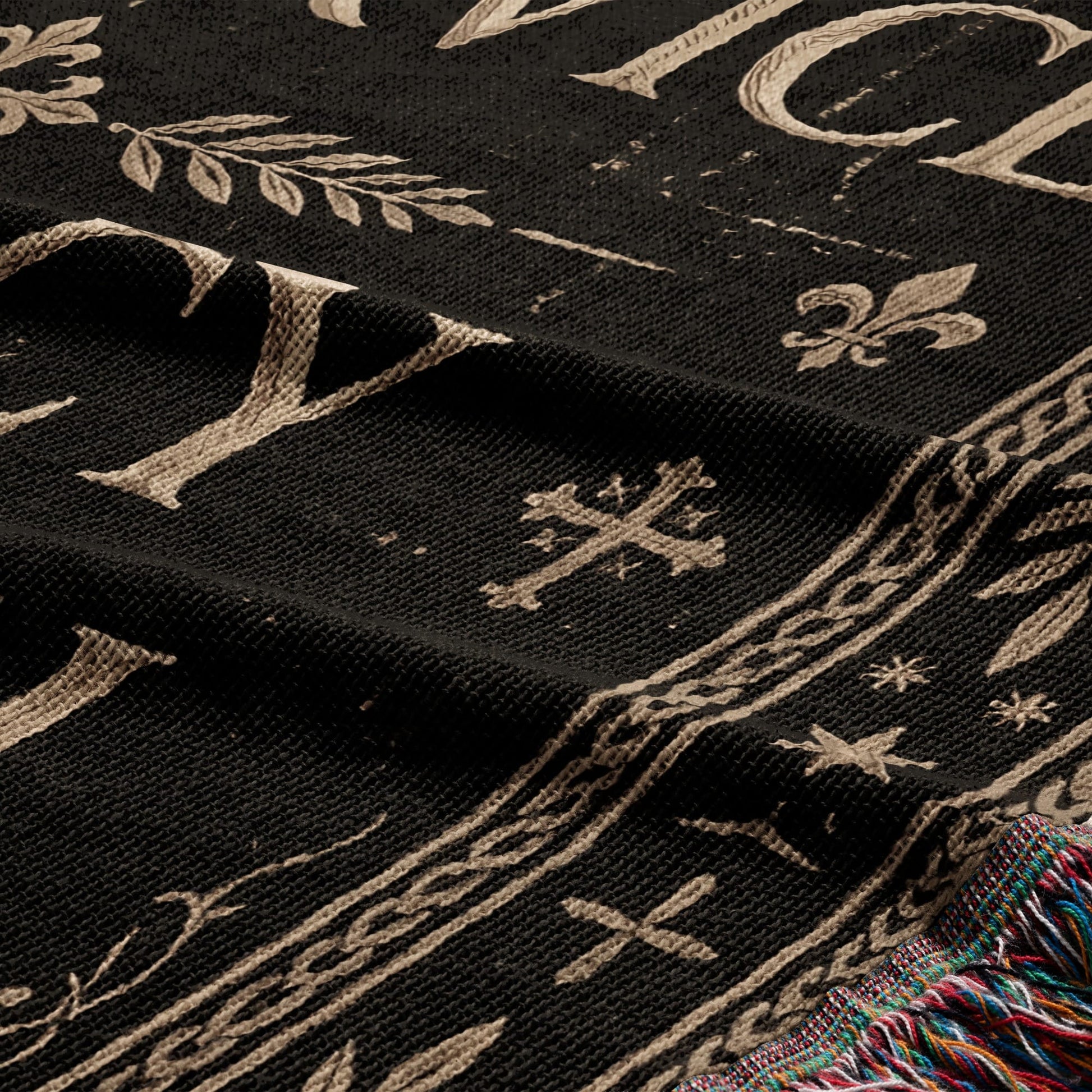 Black woven fabric with a beige fleur-de-lis and leaf pattern, and fringed edge.