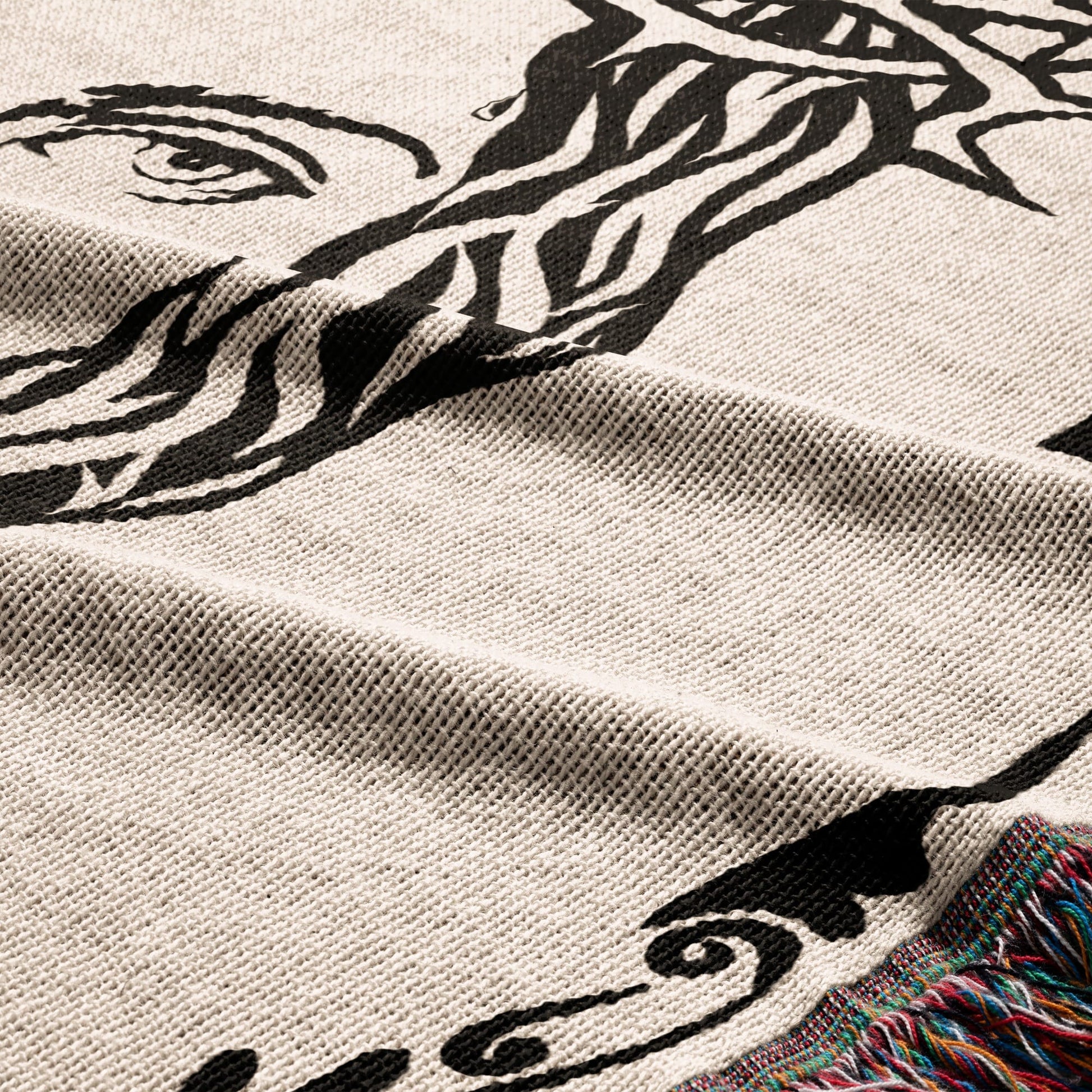 Close-up of a woven blanket with a black abstract portrait design and fringed edge.