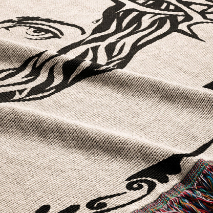 Close-up of a woven blanket with a black abstract portrait design and fringed edge.