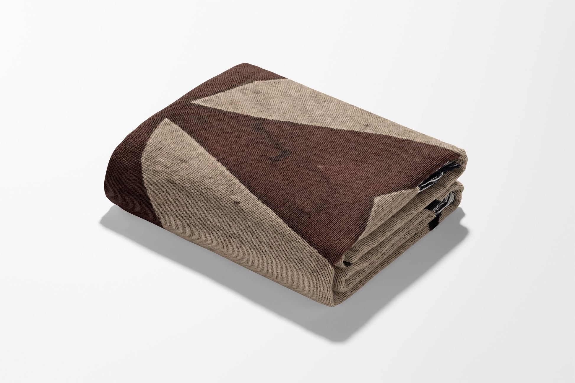 Folded blanket with geometric pattern in brown and tan on white background.