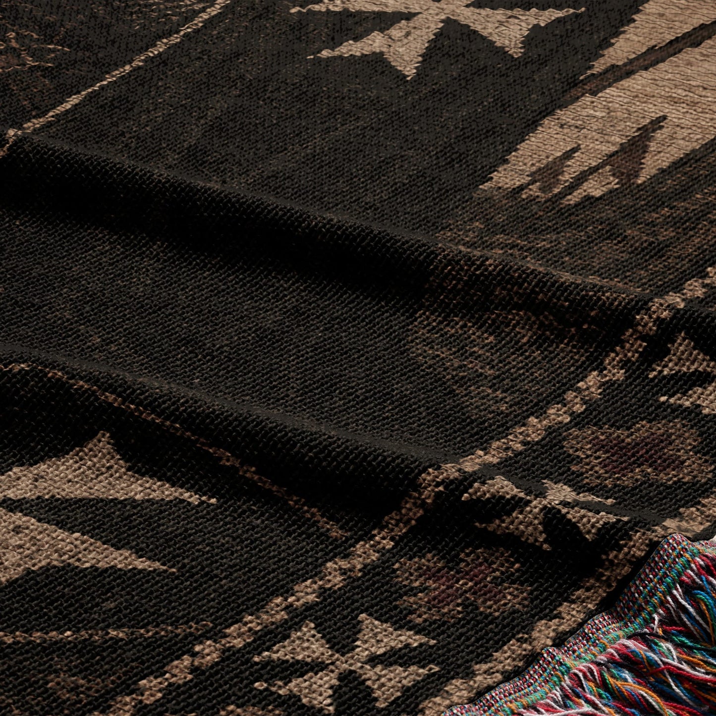 Close-up of a dark woven textile with cream geometric patterns and colorful fringe.