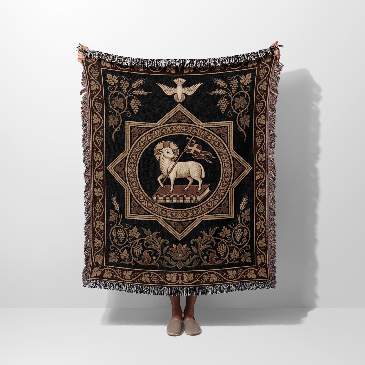 Tapestry with lamb on book and grape vine border, held by person.