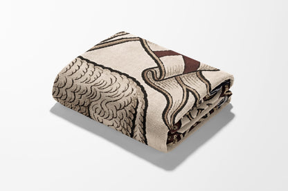 Folded beige blanket with brown and beige ornate pattern, close-up view.