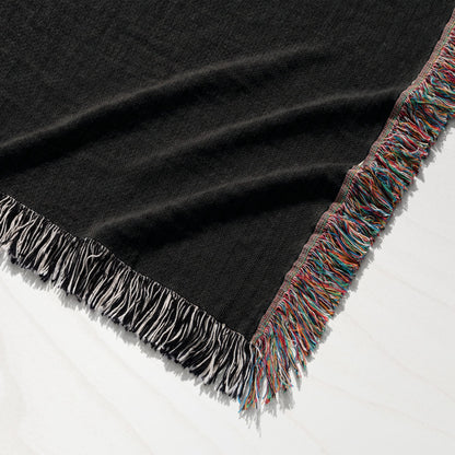 Black knit throw blanket with multicolored fringe on white background.