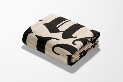 Folded blanket with large black gothic "H" pattern on cream background.