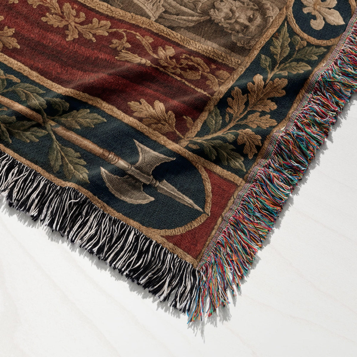 Folded woven throw blanket with medieval-style heraldic patterns, oak leaf borders, and colorful fringe edges.