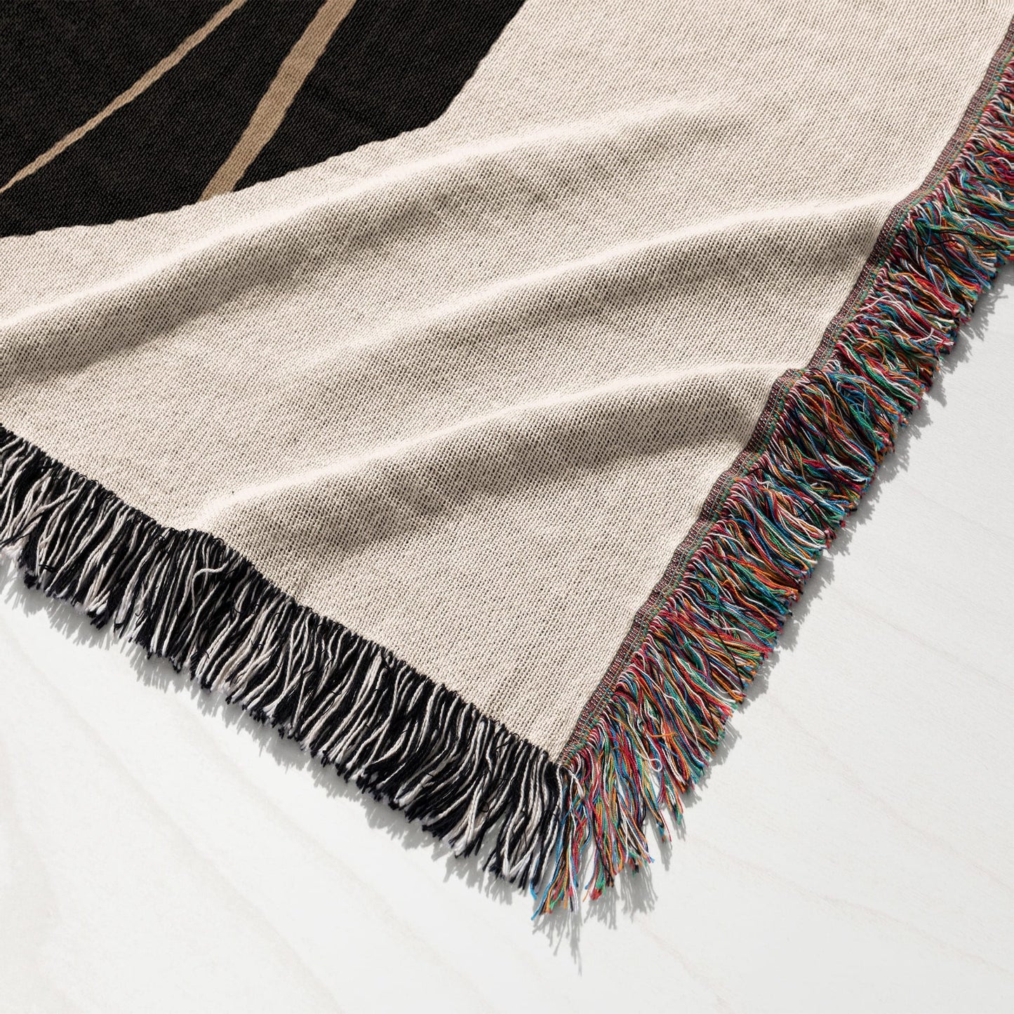 Woven throw blanket with fringe in beige, black, and multi-colored stripes.