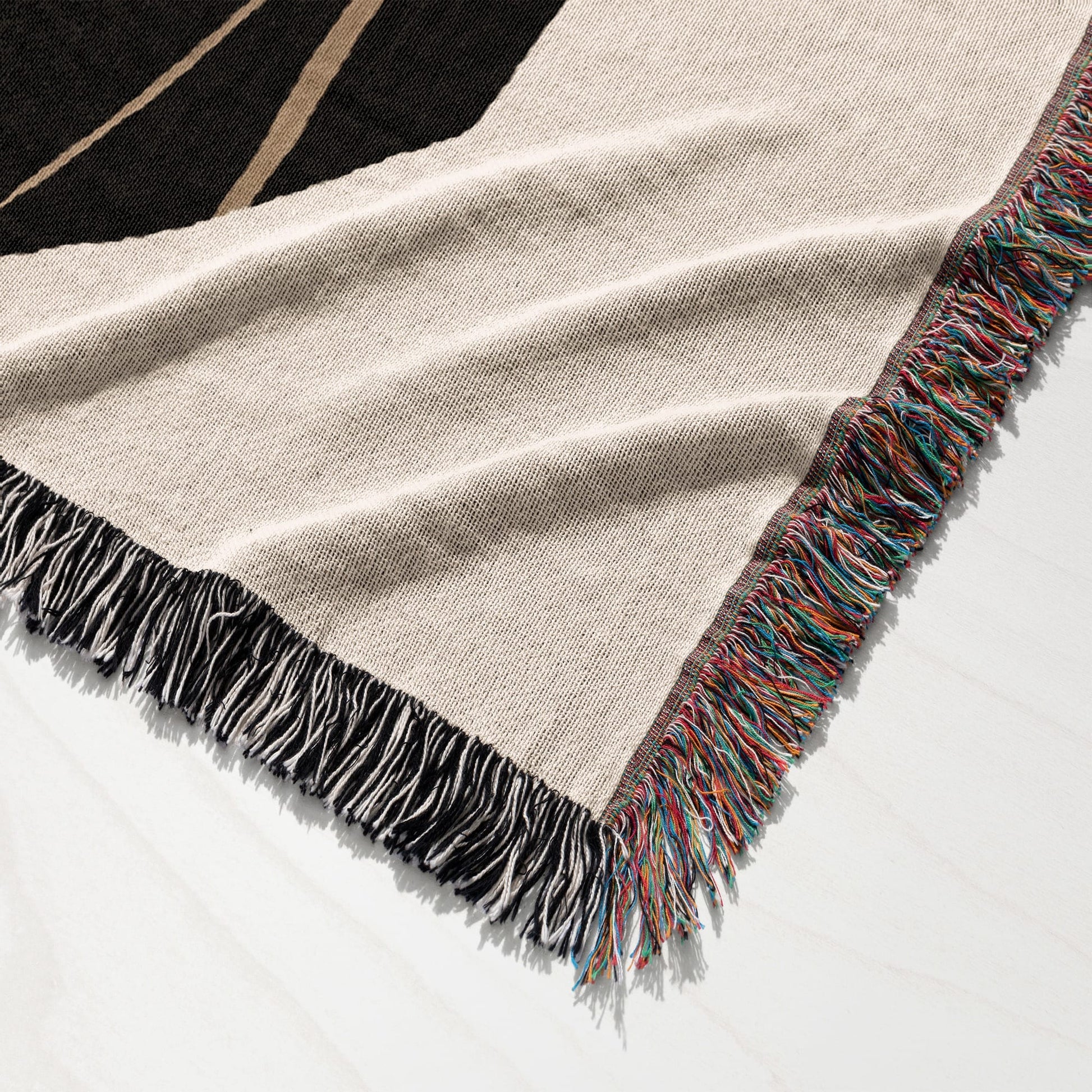 Woven throw blanket with fringe in beige, black, and multi-colored stripes.