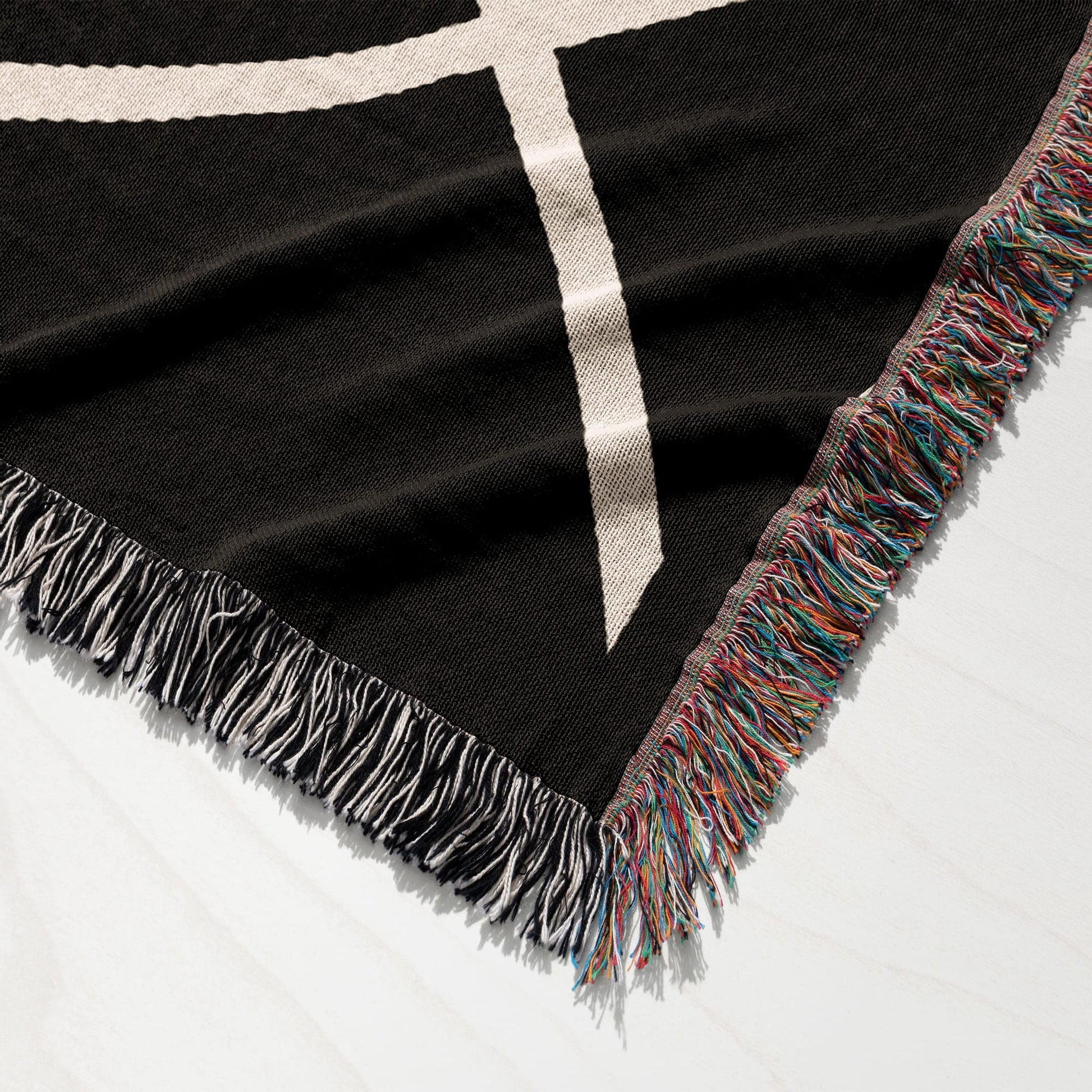 Black blanket with white geometric pattern and multicolored fringe.