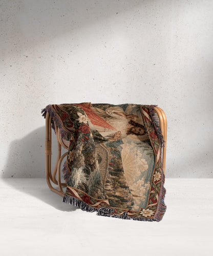 A woven tapestry blanket featuring the Divine Mercy image draped over a light wooden chair.