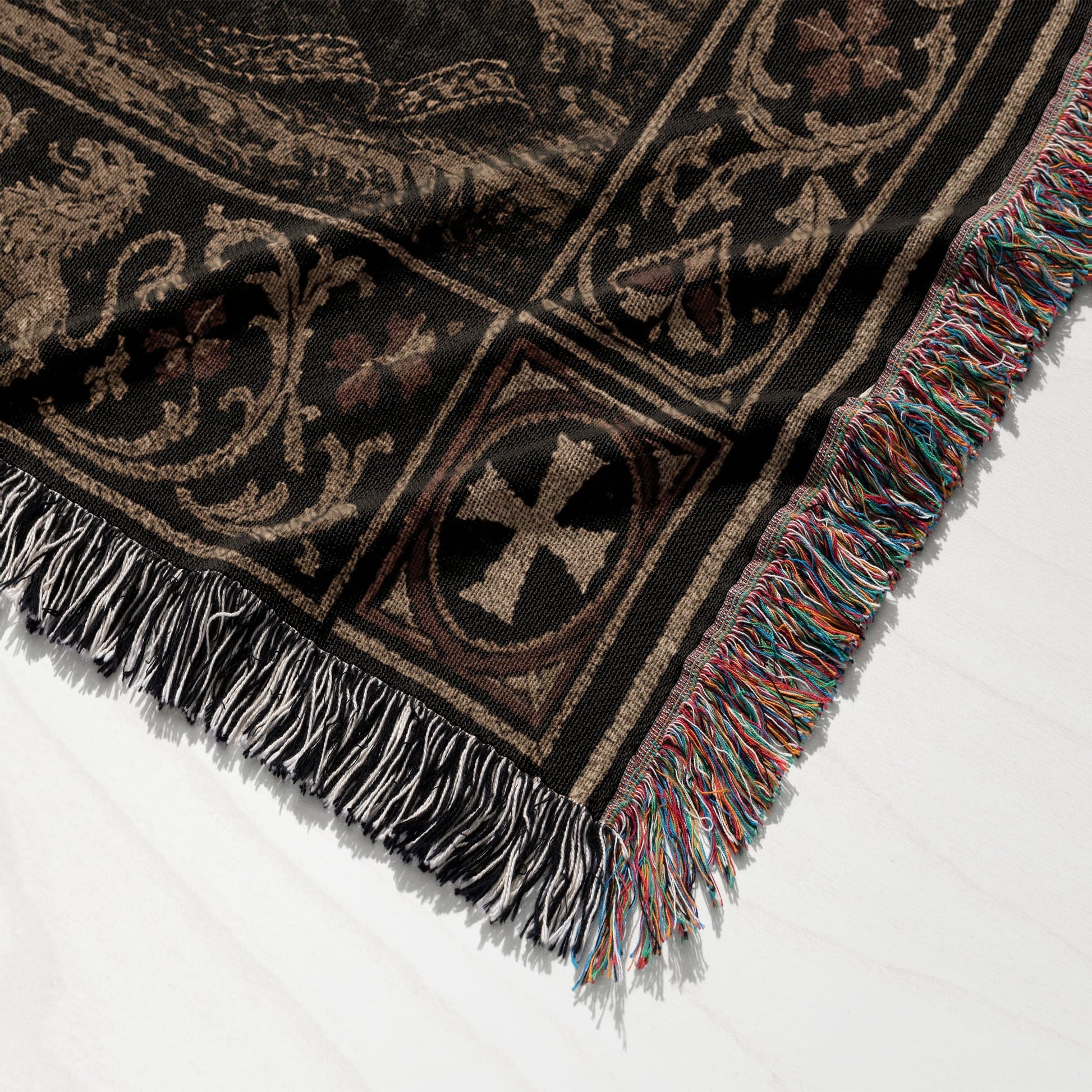 Black woven throw blanket with multicolor fringe and ornate medieval-style pattern.