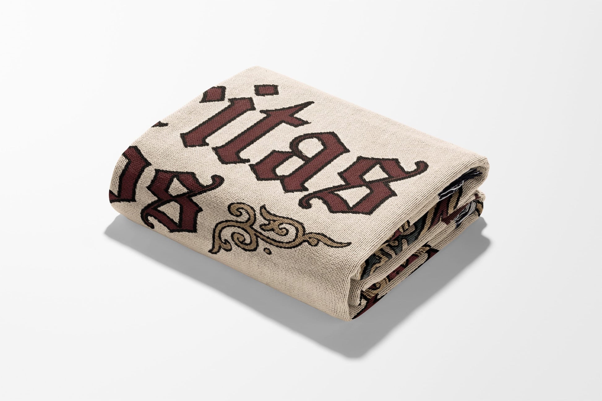 Folded cream throw blanket with gothic "itas" text and ornamental design.